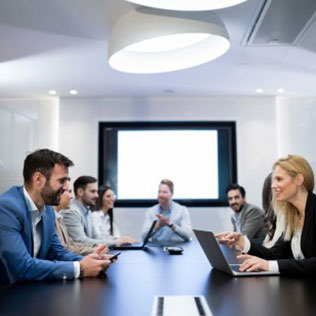 well-dressed business people sitting around a conference table with laptops talking