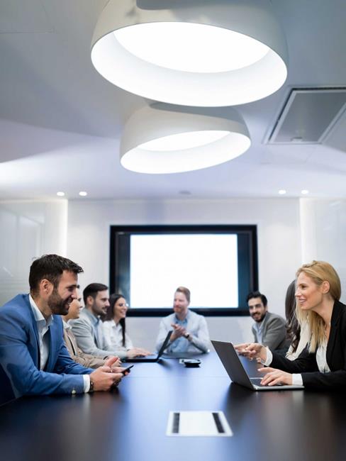 well-dressed business people sitting around a conference table with laptops talking